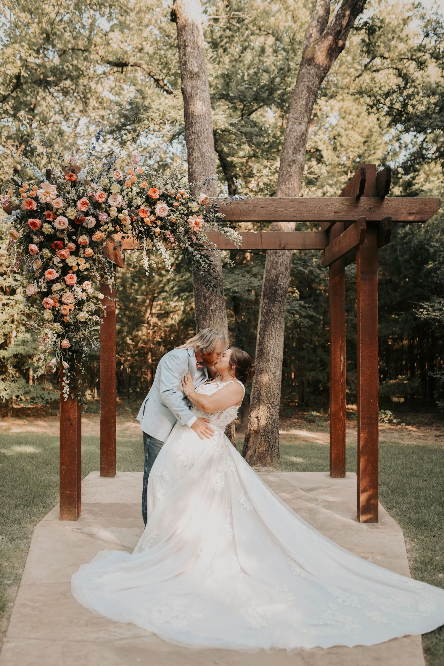 Bride leaning into groom under a wooden arch covered in roses and greenery