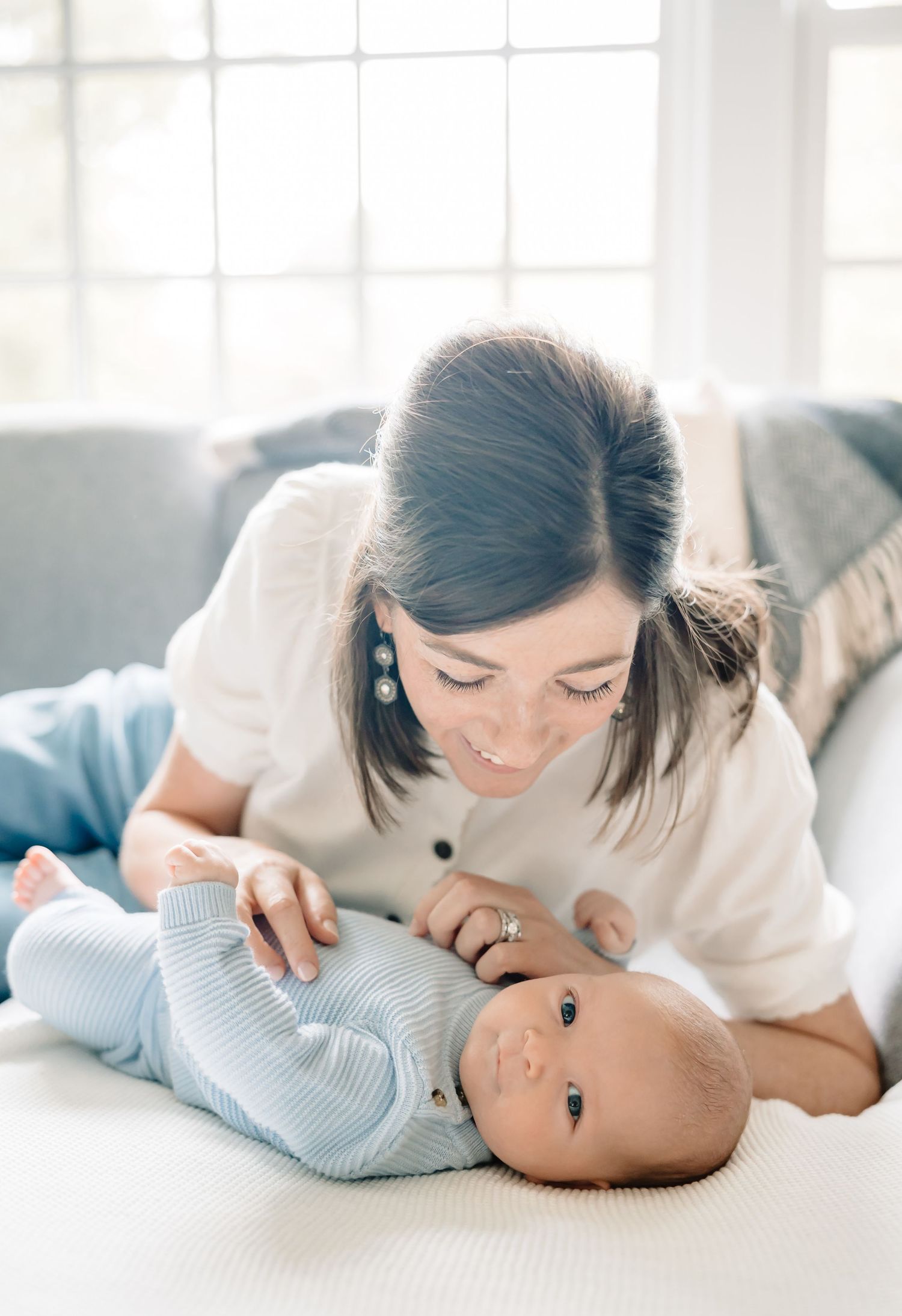 Tender moment of tenderness and bonding with a baby lying on white bedding in soft natural window light.