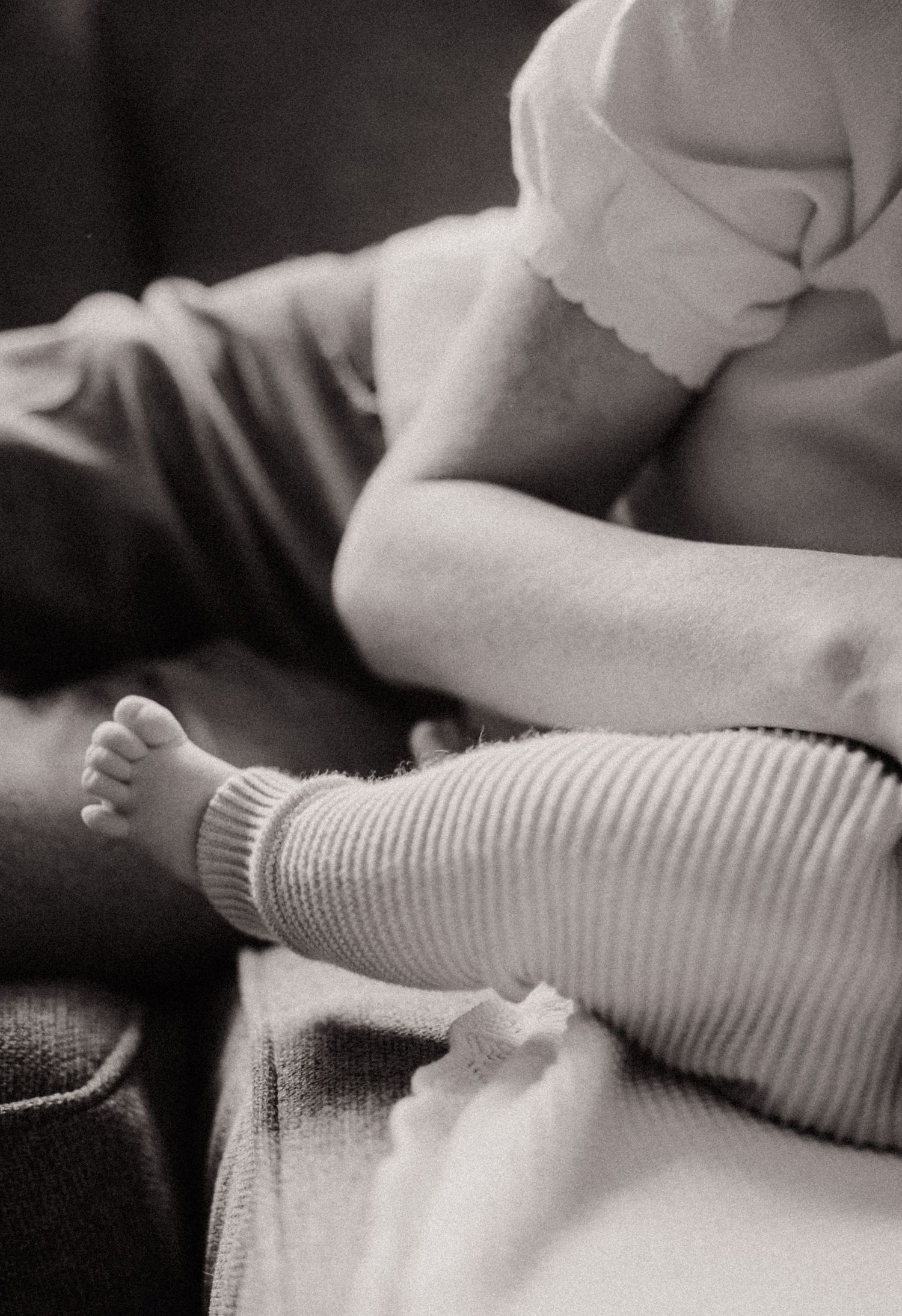 Black and white close-up of baby legs wearing ribbed white leggings while resting on a couch.