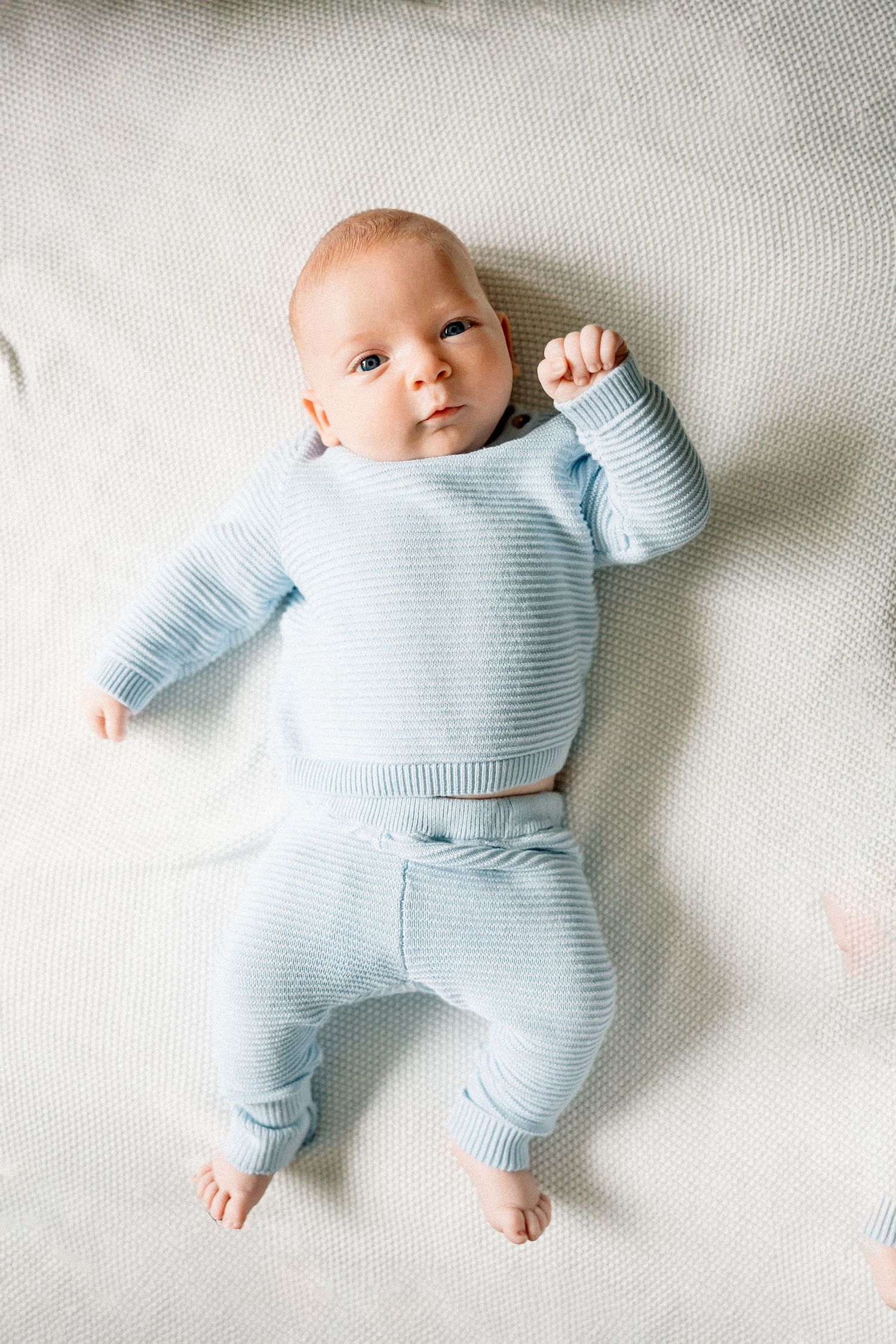Baby wearing soft light blue ribbed sweater and pants outfit lies on white textured surface.