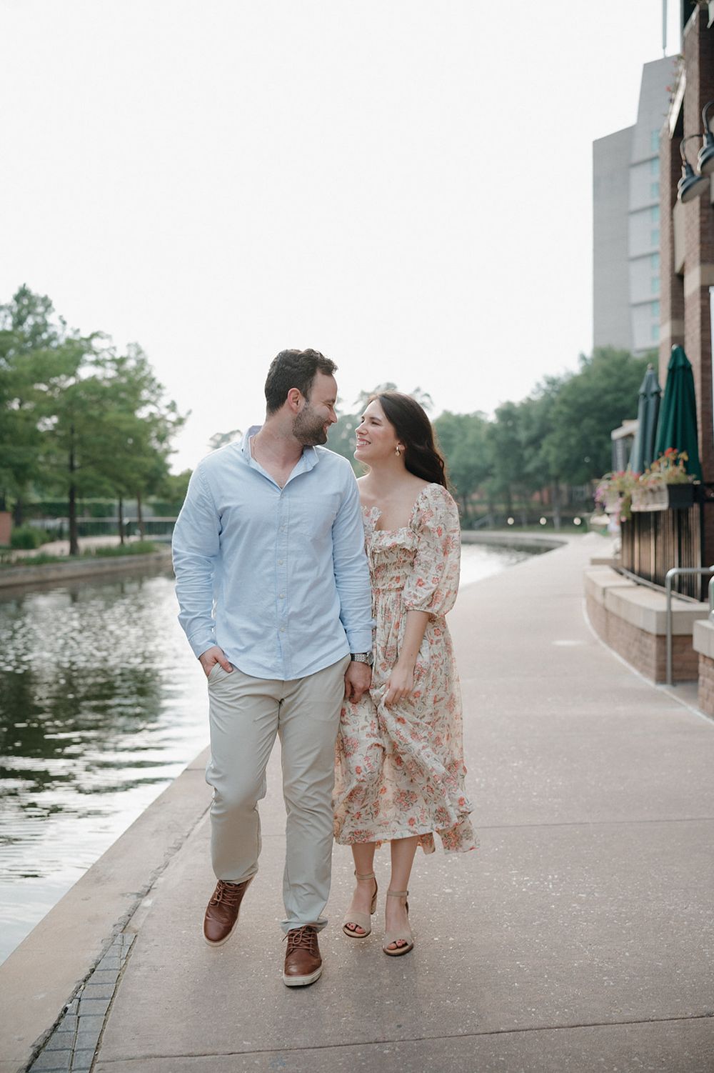 A couple shares a romantic moment while walking along a waterfront promenade on a peaceful afternoon.