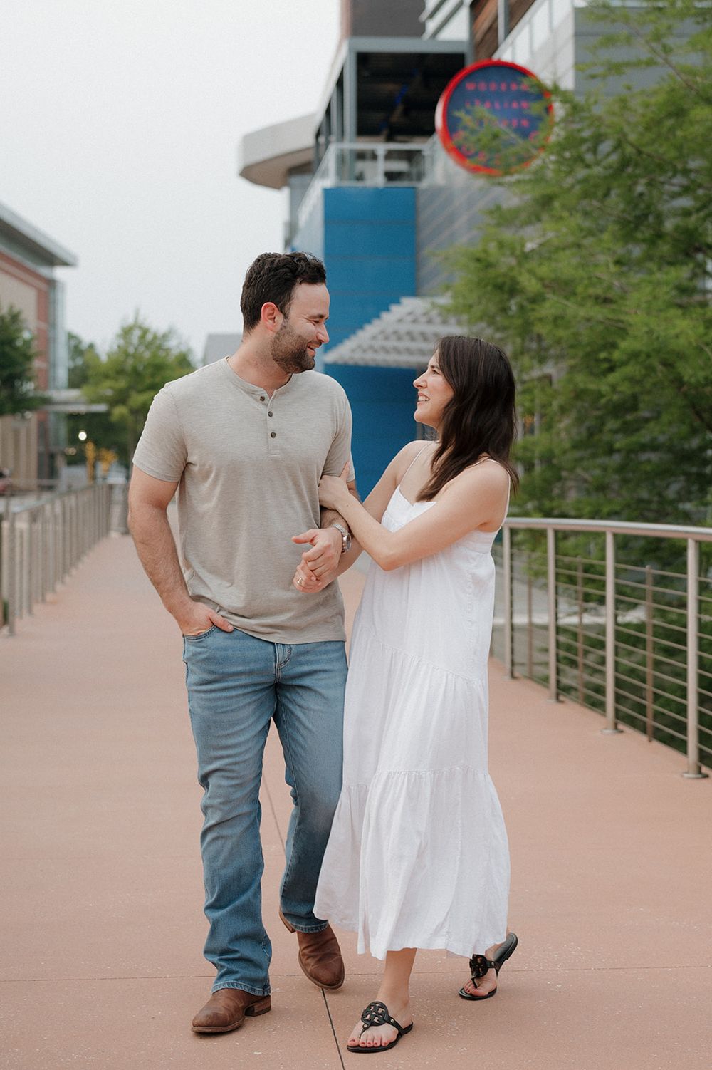 Couple walking and smiling together on an urban pathway wearing casual summer outfits.