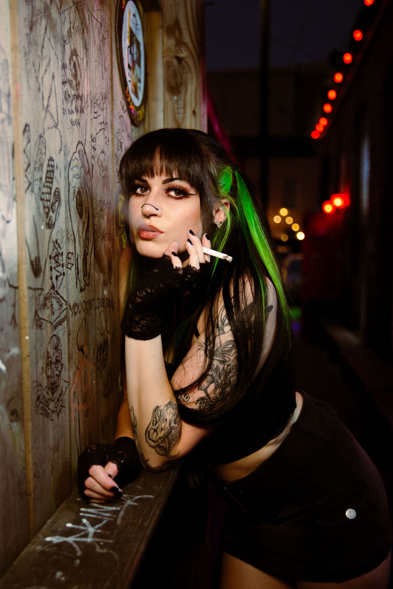 A person in edgy street fashion poses by neon-lit window blinds casting vibrant red and blue lighting effects.