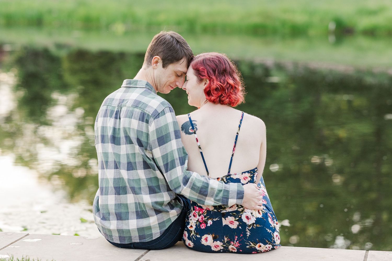 Couple in casual attire sitting close together by a serene pond on a sunny afternoon at Cantigny Park