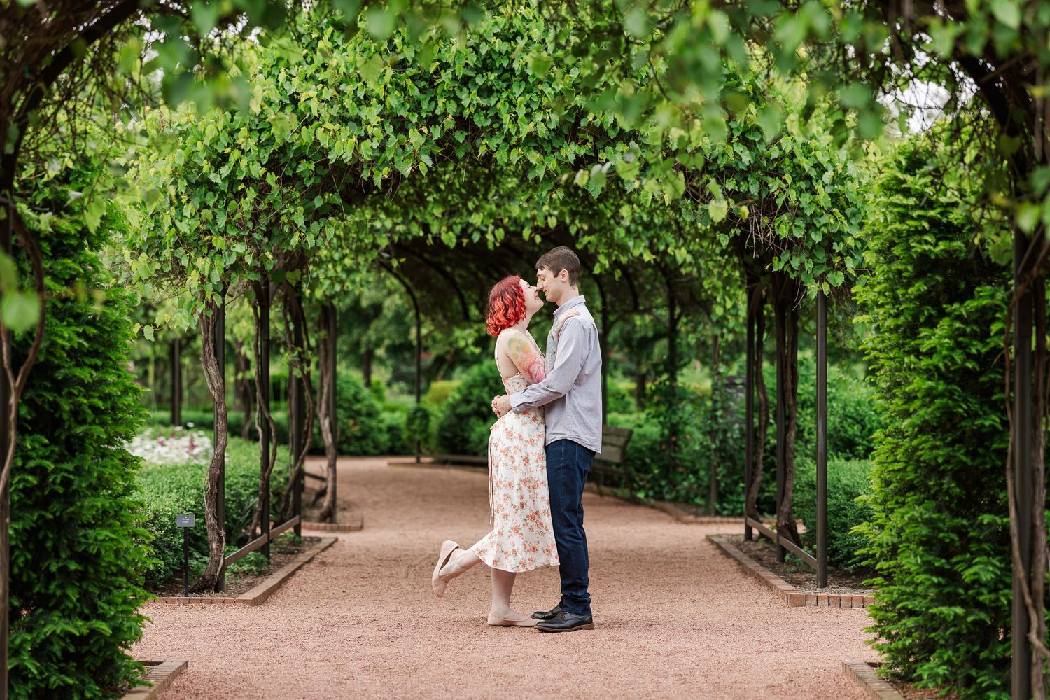 A romantic couple shares a tender moment under a lush green garden arbor on a stone pathway in summer at Cantigny Park
