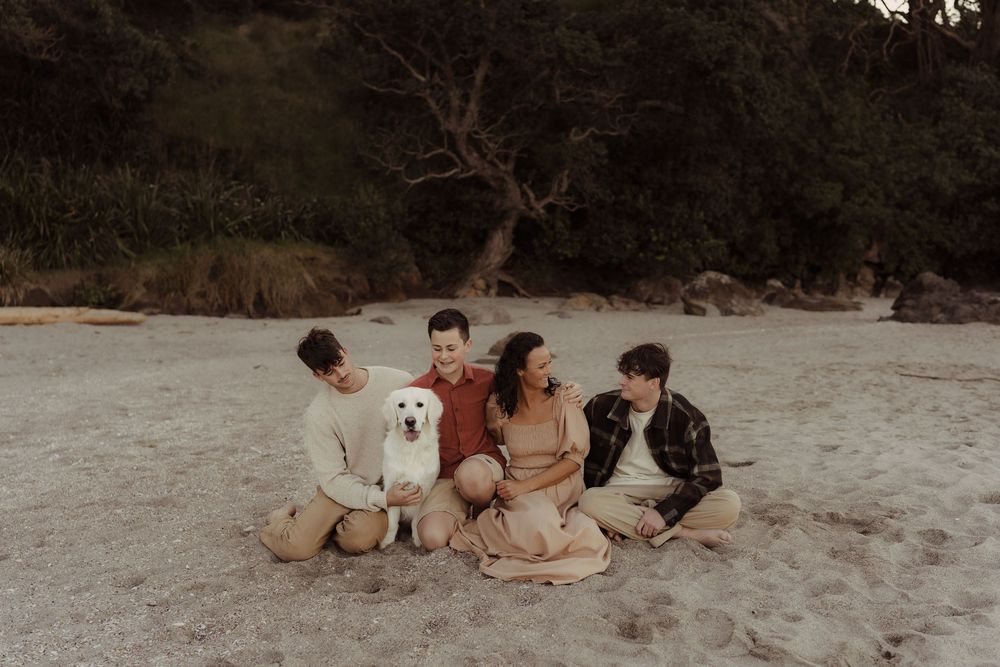 A white labrador sits with group on sandy beach during sunset with trees in background.