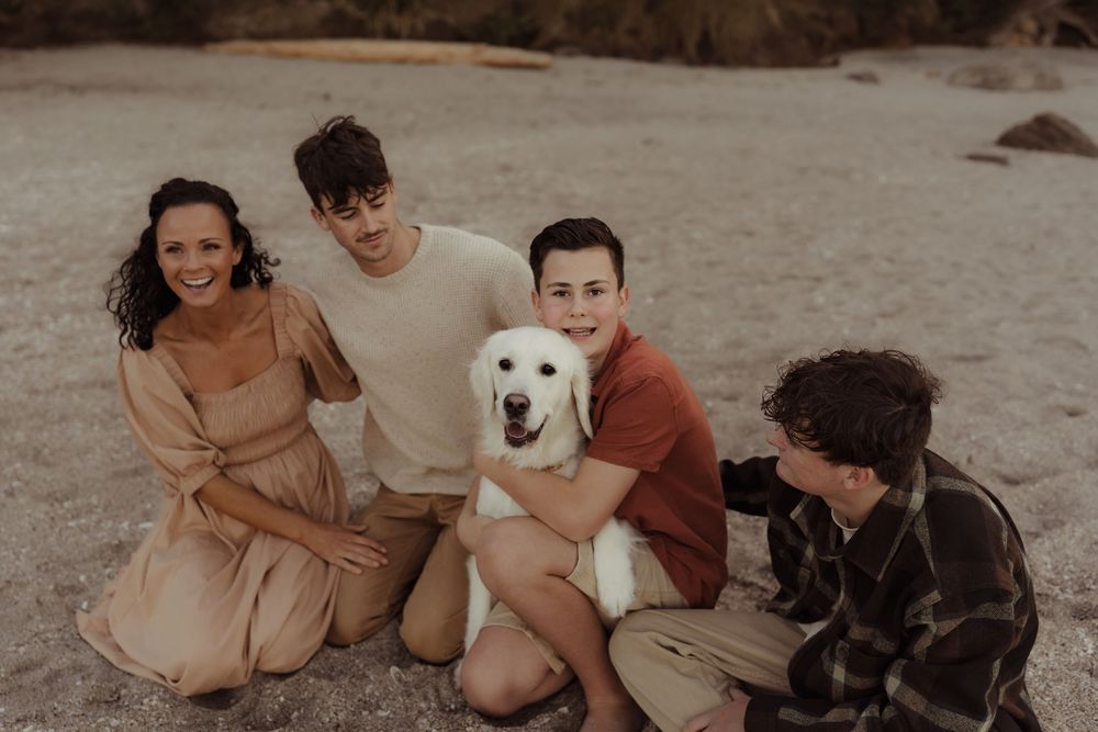 A group relaxes on a beach with their friendly white labrador retriever during golden hour.