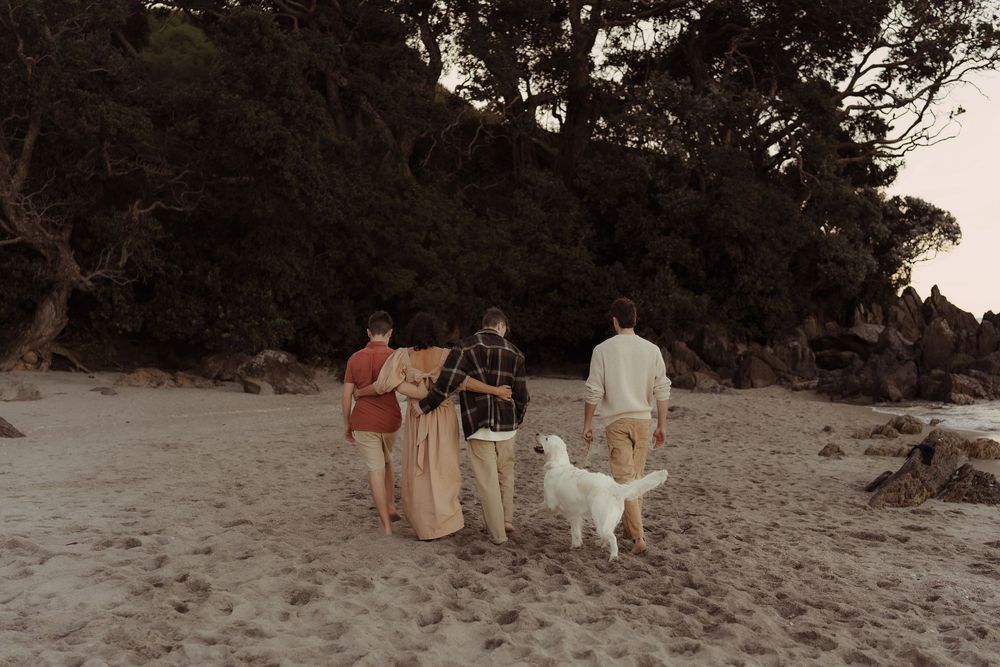 Family and pet dog walking together on a sandy beach path during sunset.