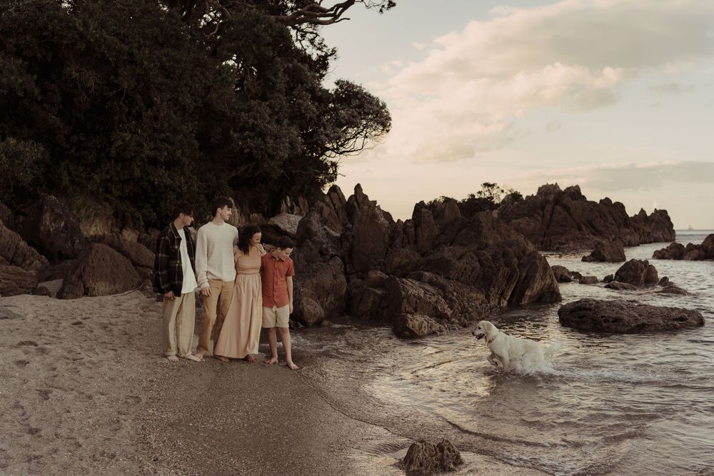 Group walking along rocky coastline with waves crashing against shore during golden hour.