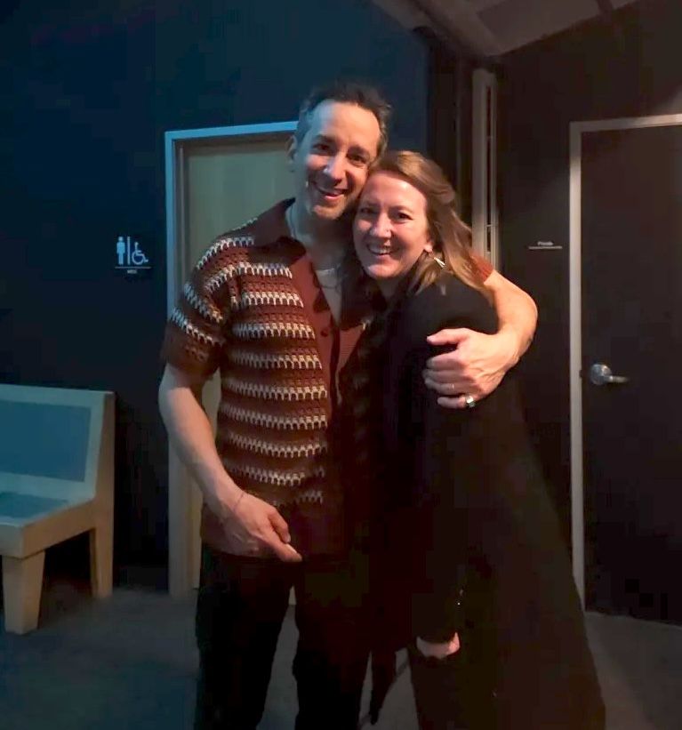 Two people embracing and smiling warmly together in a dimly lit room wearing casual attire.