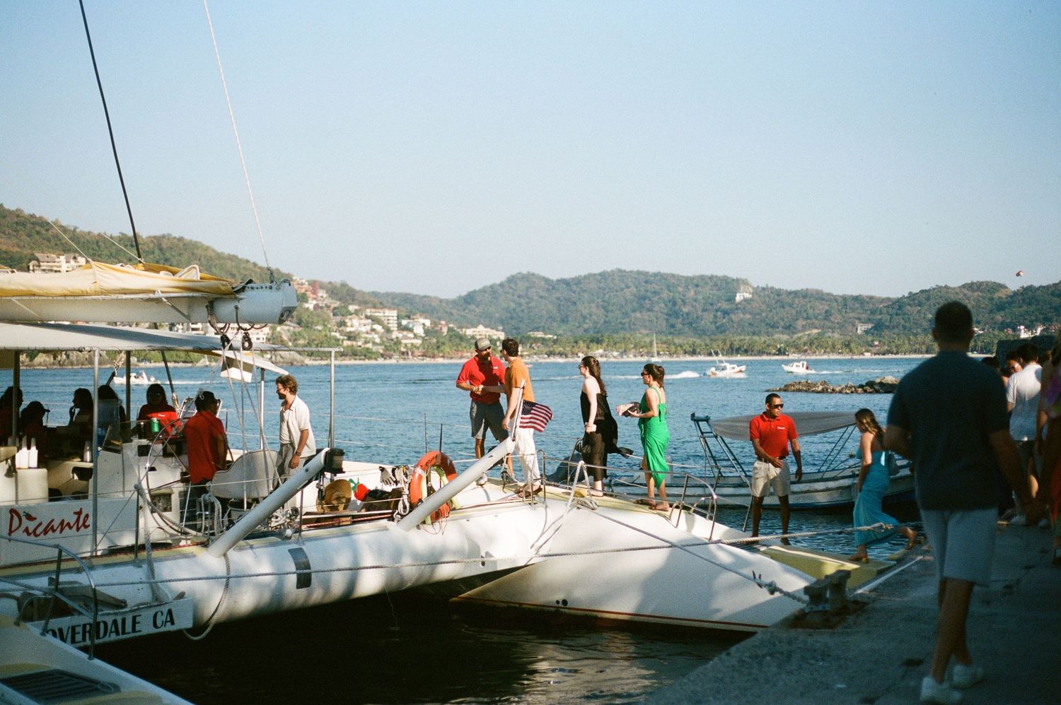Sailboat party with multiple guests on deck in a scenic bay setting.