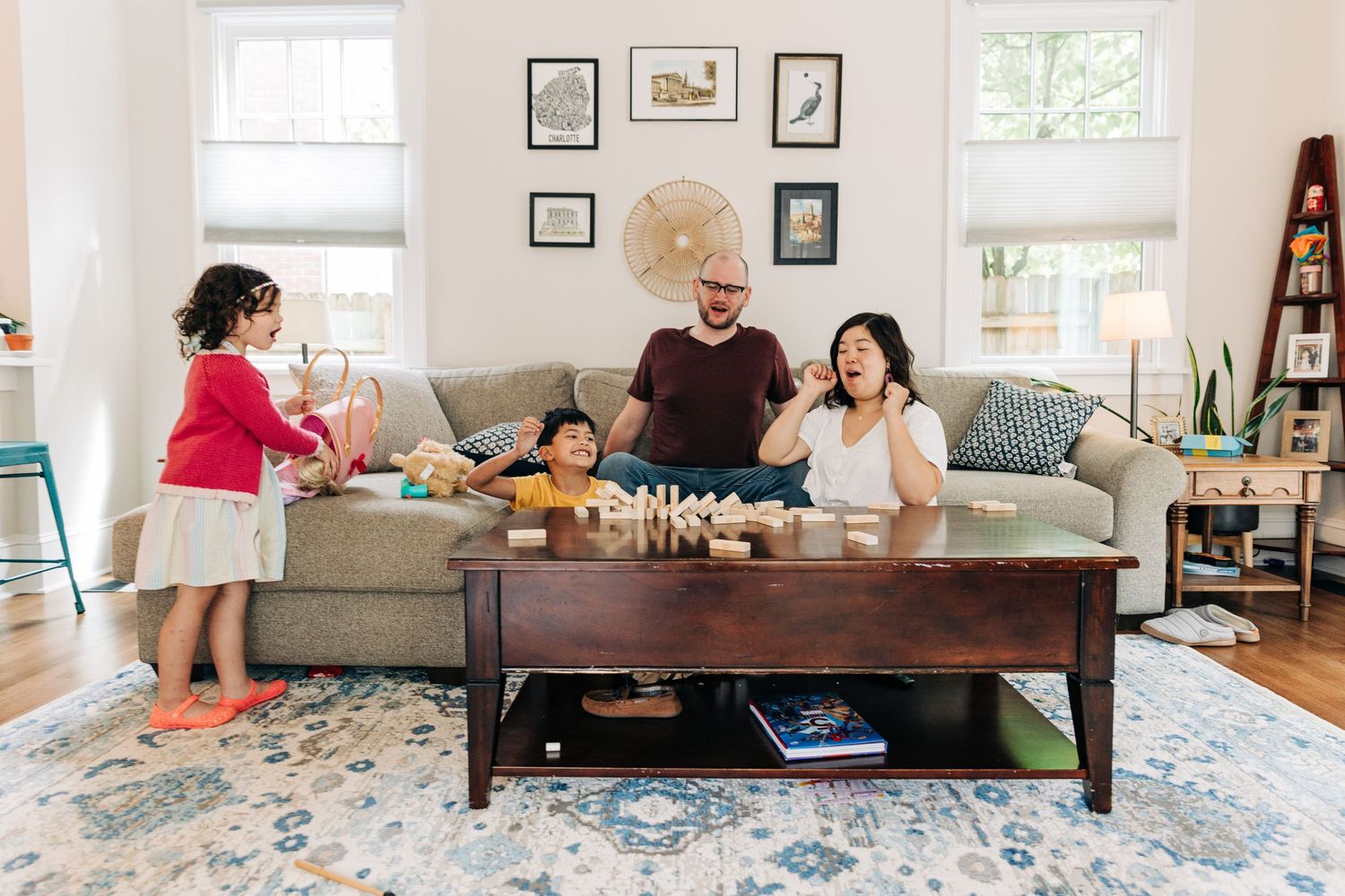 A family gathers in their bright living room around a coffee table to play a board game in a cozy setting.