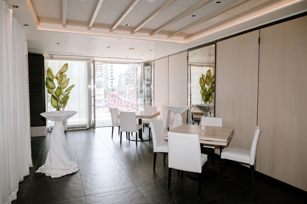 Modern white dining space with upholstered chairs, dark flooring, and potted plants in a bright minimalist interior.