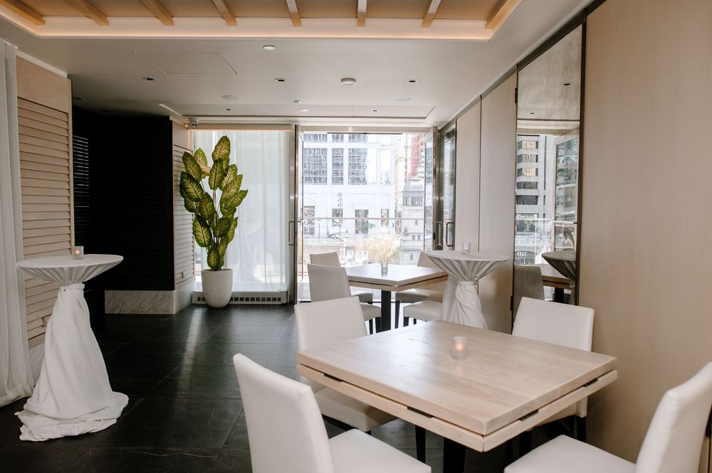 Modern dining space with white chairs, marble tables, and a tall fiddle leaf fig plant in a sleek urban interior.