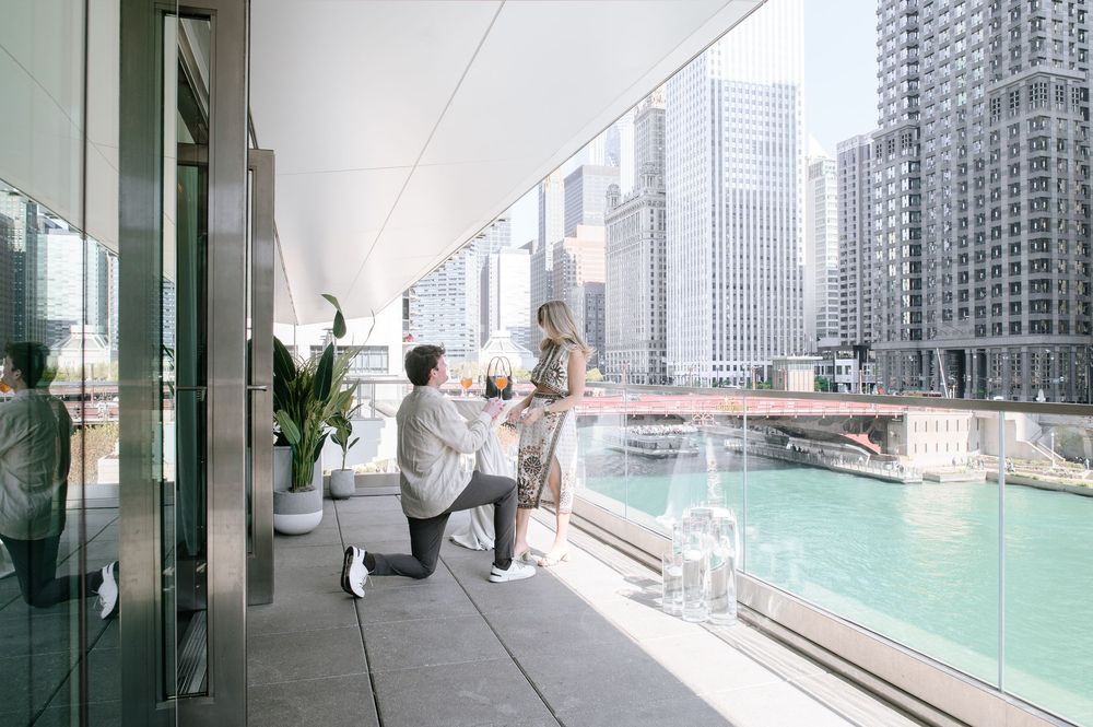 Modern balcony overlooking bright turquoise river with high-rise buildings and glass railings in urban setting.