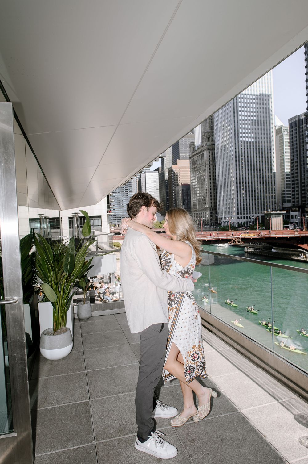 A couple shares a romantic moment on a balcony overlooking the Chicago River with city skyscrapers in the background.