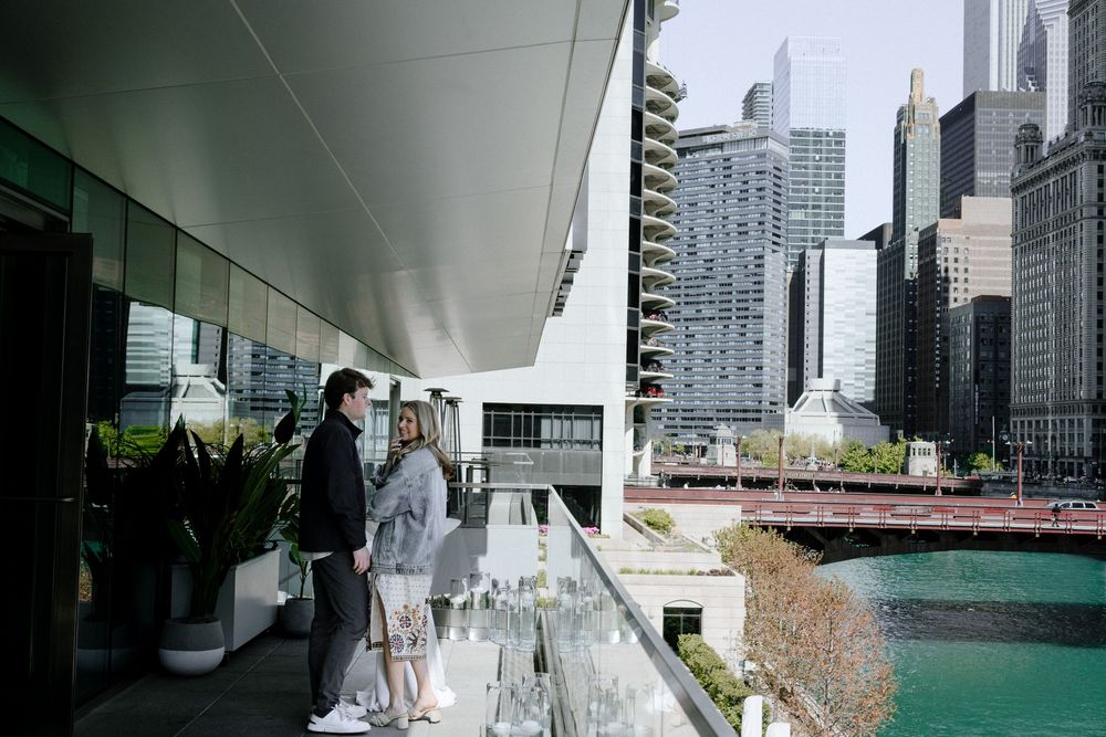 People standing on a stylish outdoor terrace with modern skyscrapers and river views in an urban setting.