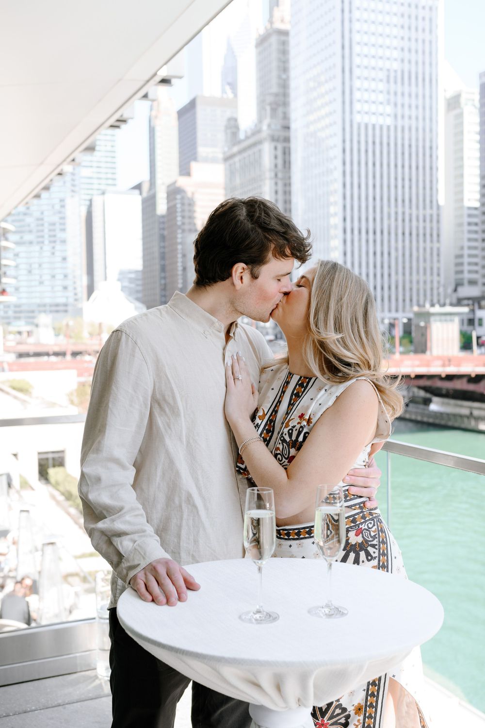 A romantic couple shares an intimate moment on a rooftop terrace overlooking the Chicago River and downtown skyscrapers.