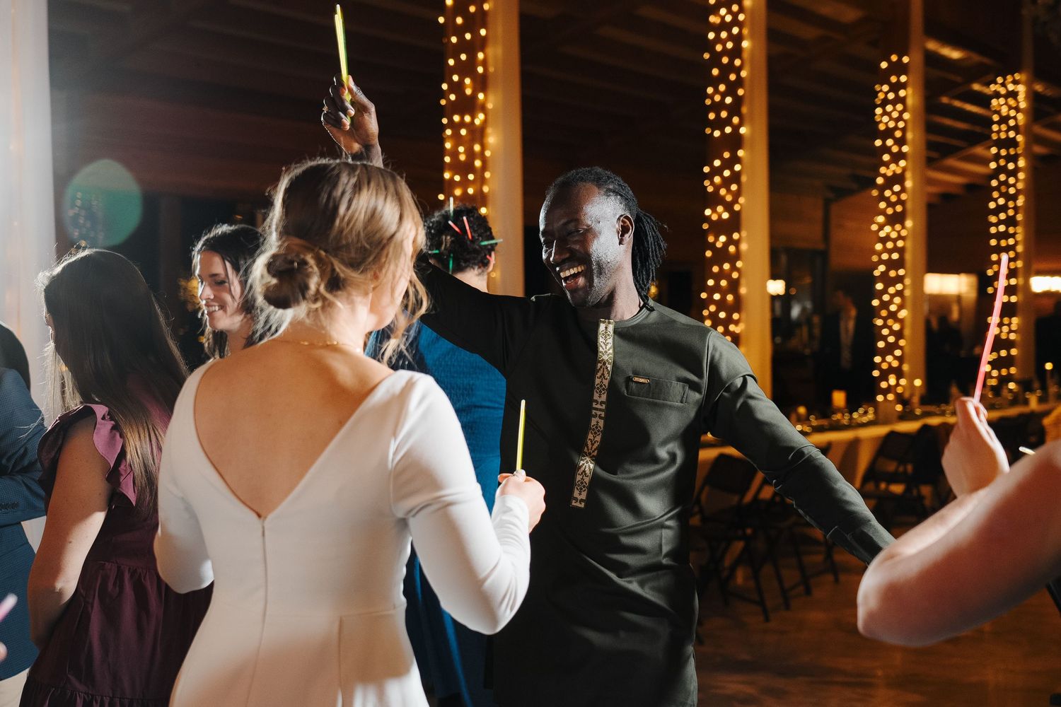 Glowing string lights illuminate a wedding reception dance floor as guests enjoy dancing and celebration.