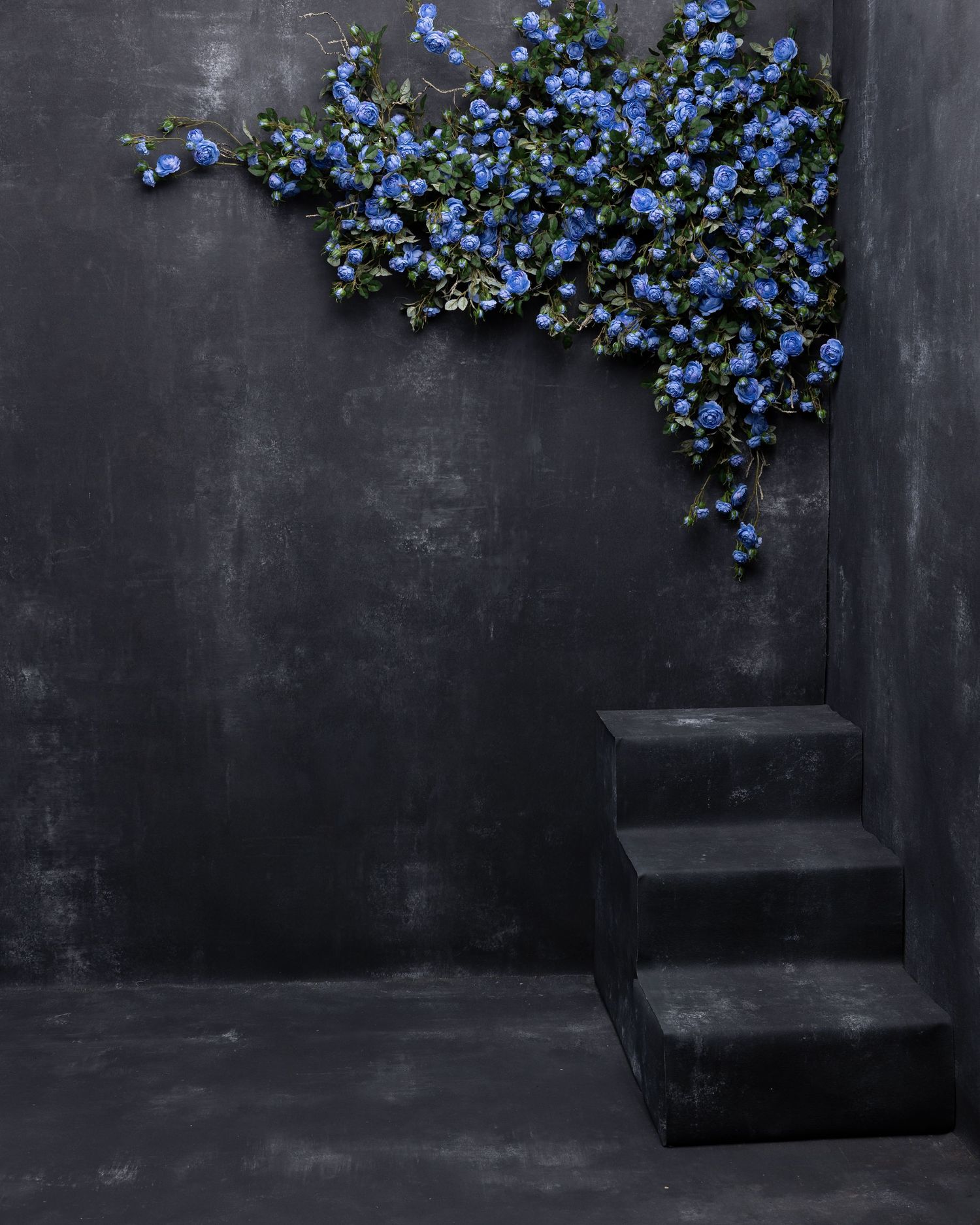Yellow flowers cascading from the top corner against a dark gray wall in a moody corner setting.