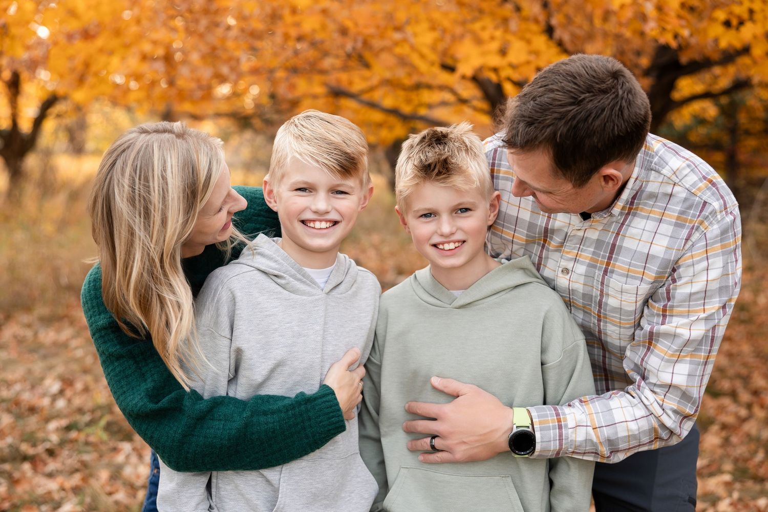 A family of four sharing a joyful moment together outdoors during autumn with golden foliage in the background.