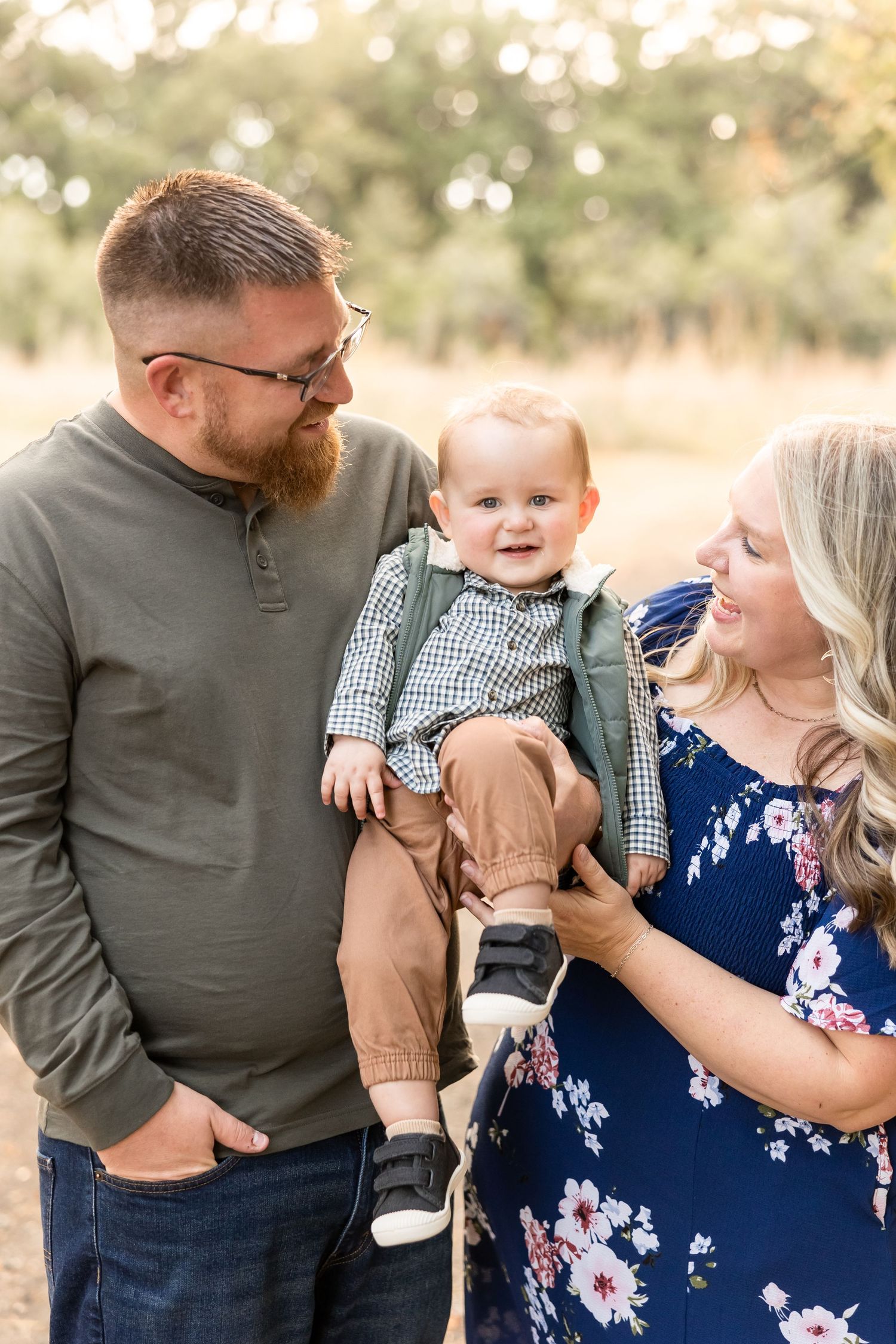 Young family in casual attire poses together outdoors in a warm autumn setting with natural bokeh background.