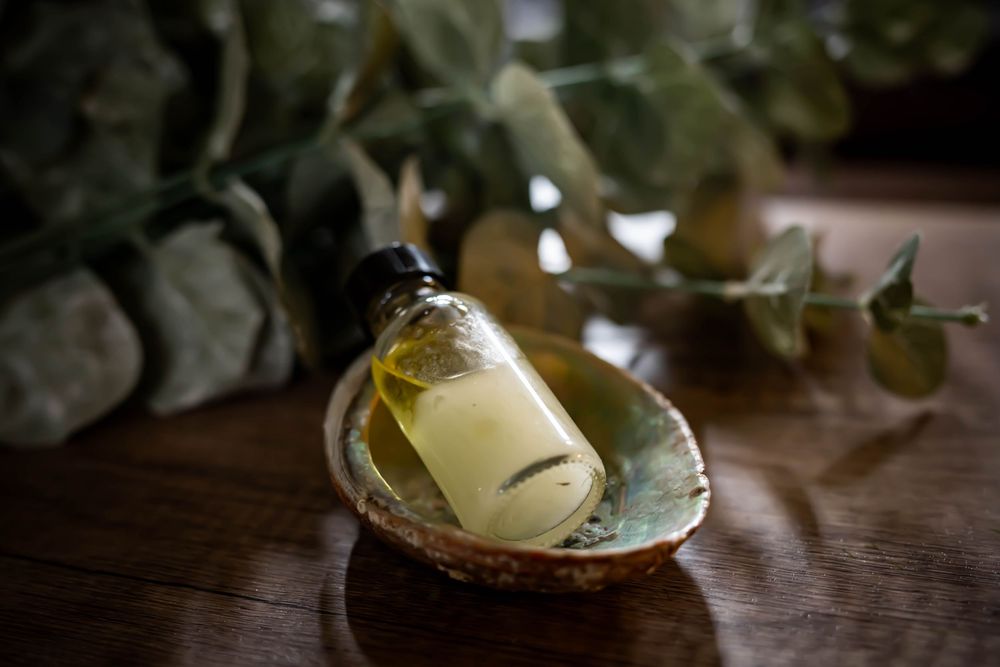 A glowing yellow potion or perfume bottle sits on an ornate ceramic plate with delicate foliage in the background.