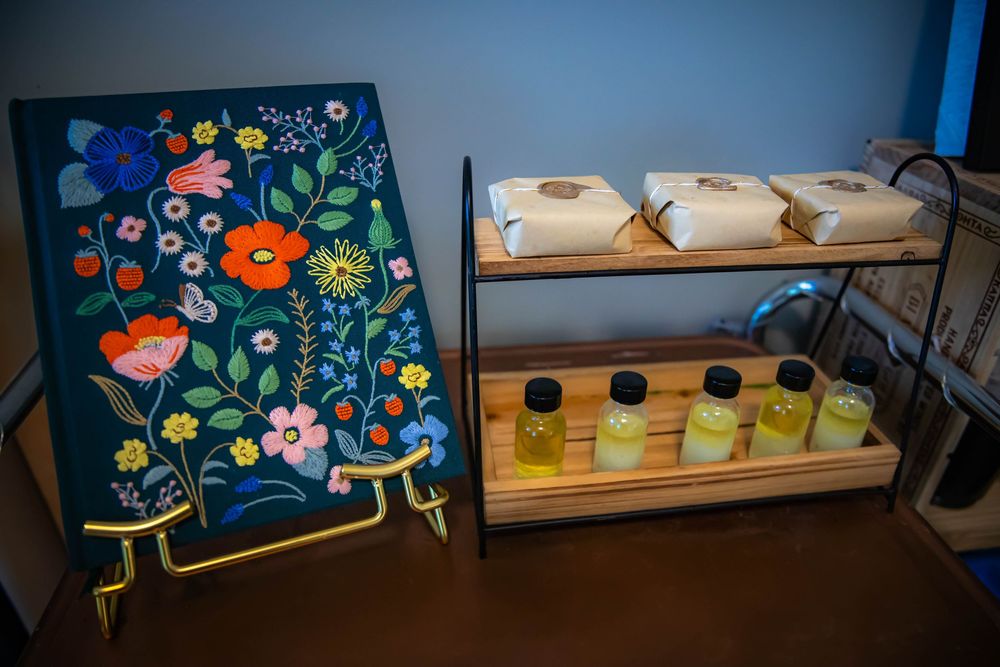 Colorful floral art display alongside wooden shelves holding glass bottles with juices at a retail counter.