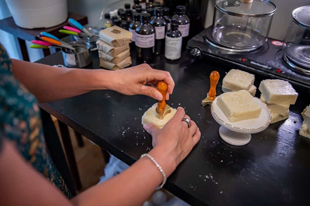 Someone carefully prepares a homemade bath bomb on a dark countertop surrounded by ingredients and supplies.