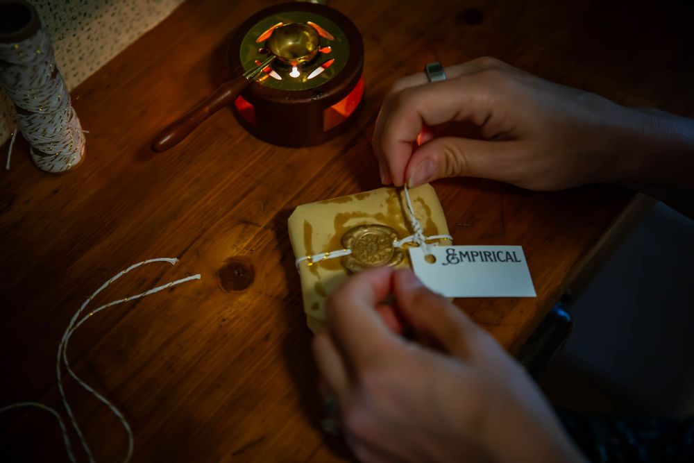 Close-up of hands attaching a label to a small wrapped package on a wooden surface.
