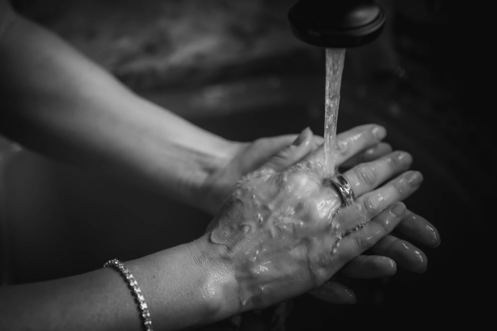 Water running over hands with a bracelet in dramatic black and white lighting.