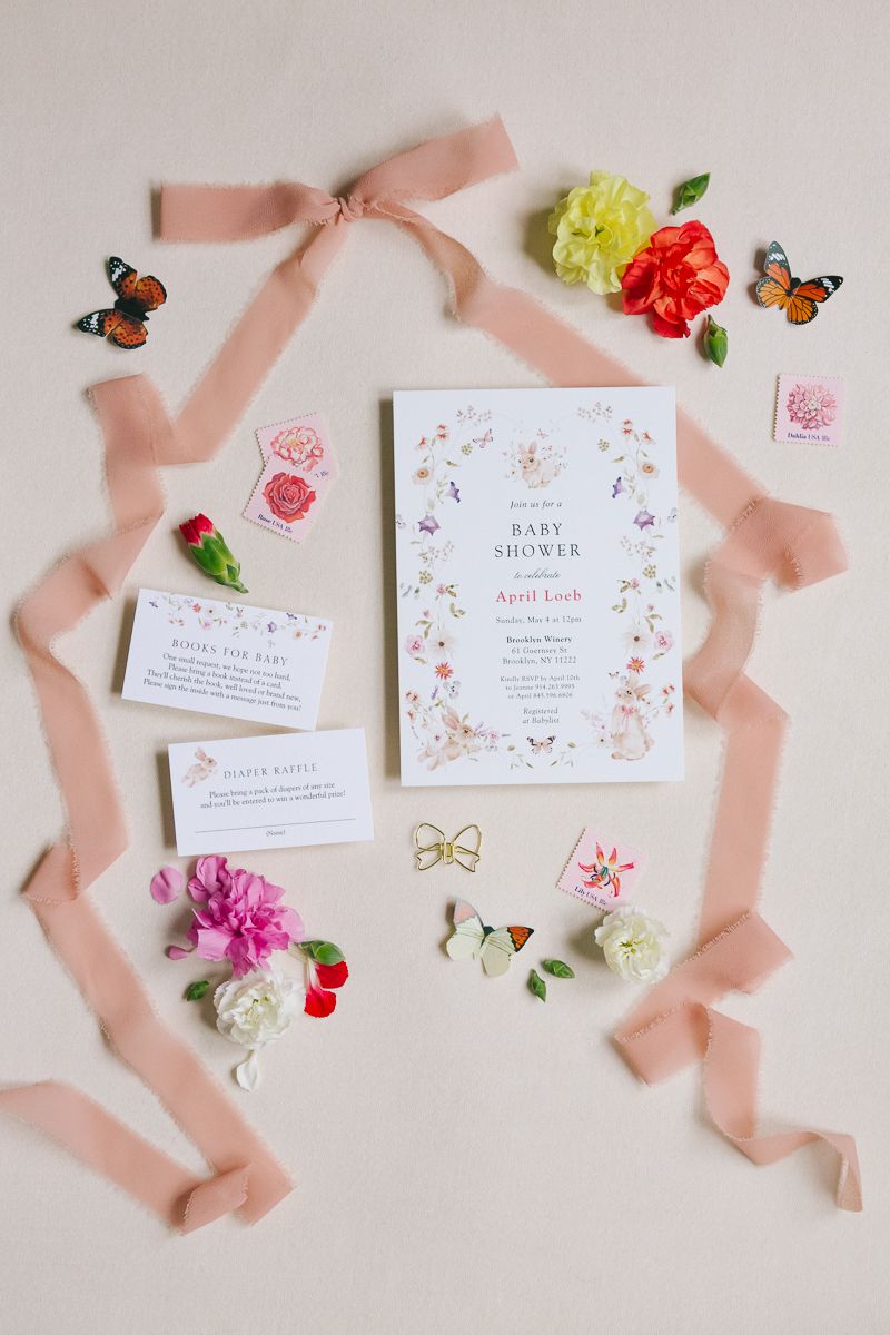 Elegant baby shower invitation flat lay with floral and butterfly accents, captured by NYC baby shower photographer Paula Brearley.