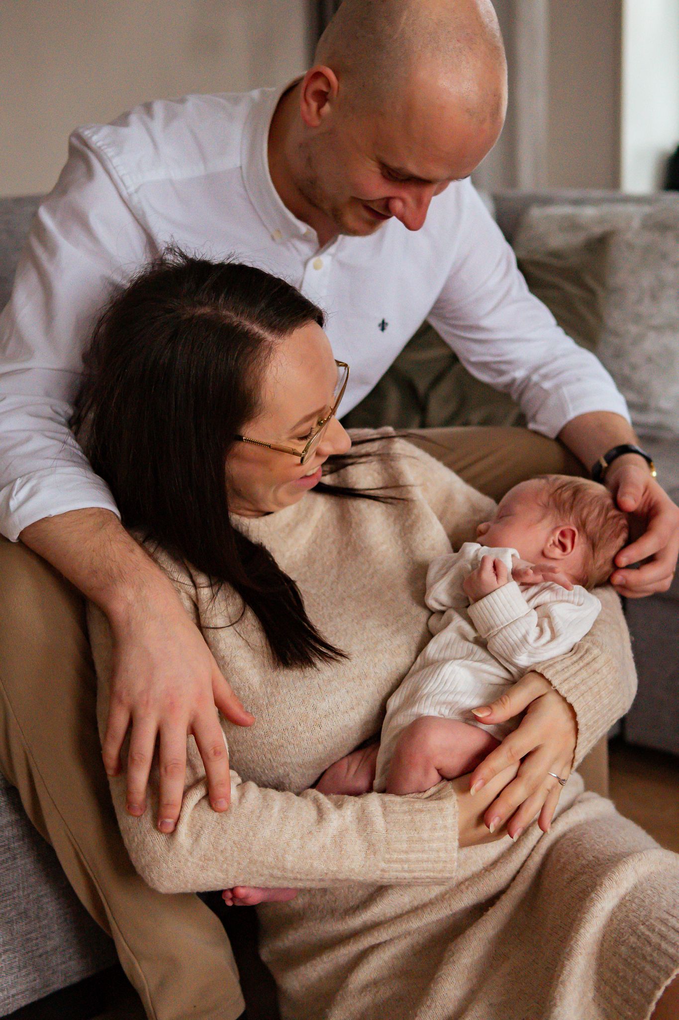 Nyblivna glada föräldrar har sin nyfödda bebis i famnen när de sitter kärleksfullt i en soffa. Fotograf, nyföddfotograf, Umeå, Västerbotten