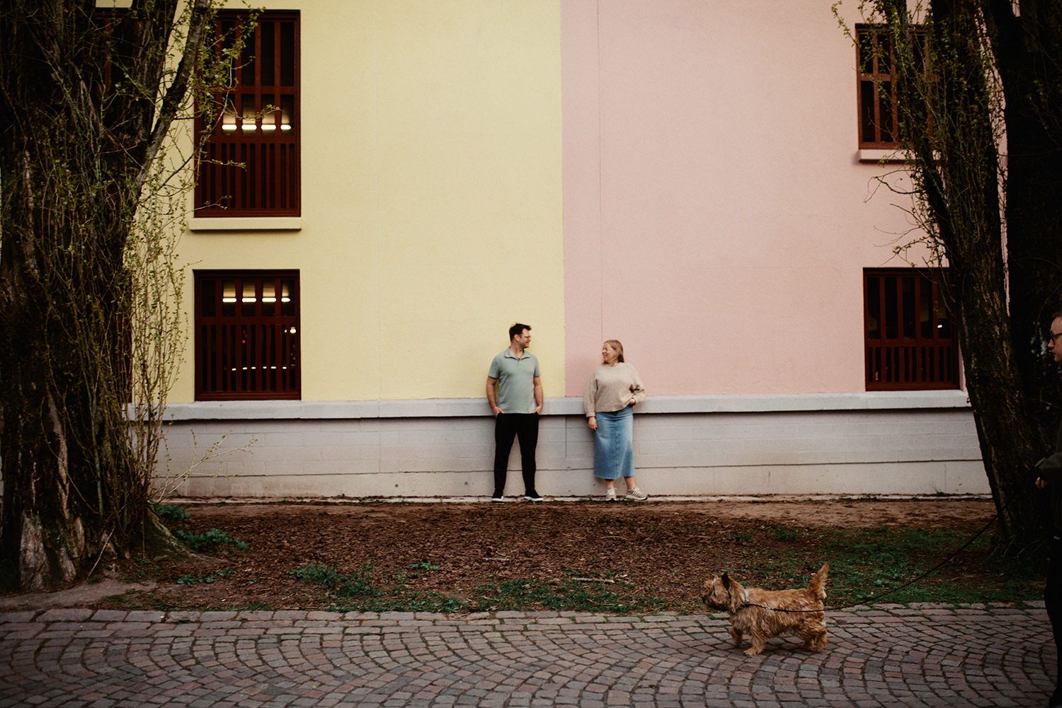 A romantic couple shares a tender kiss at sunset on a balcony overlooking an urban setting.