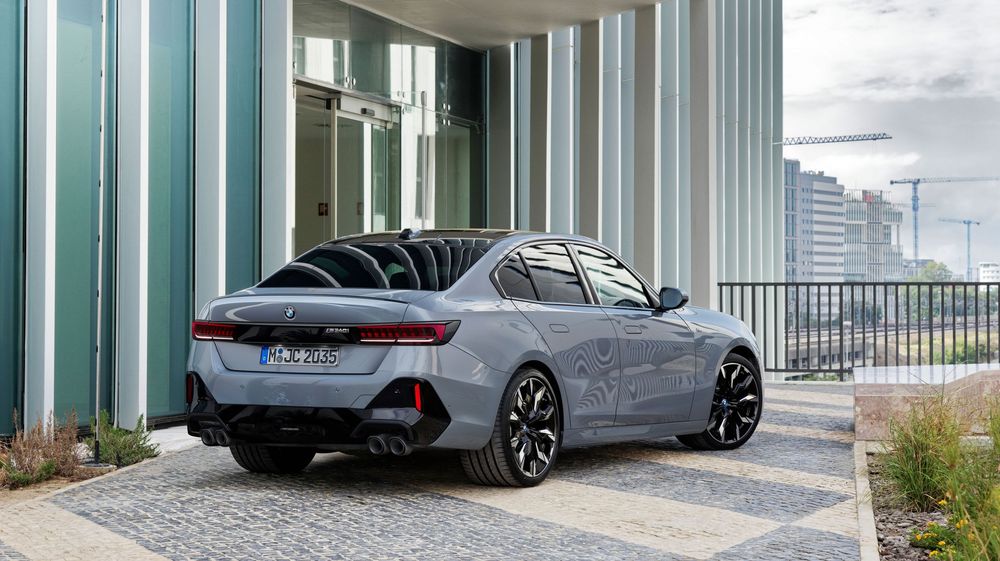 A sleek BMW M8 Gran Coupe in silver parked in front of a modern building with vertical glass panels.