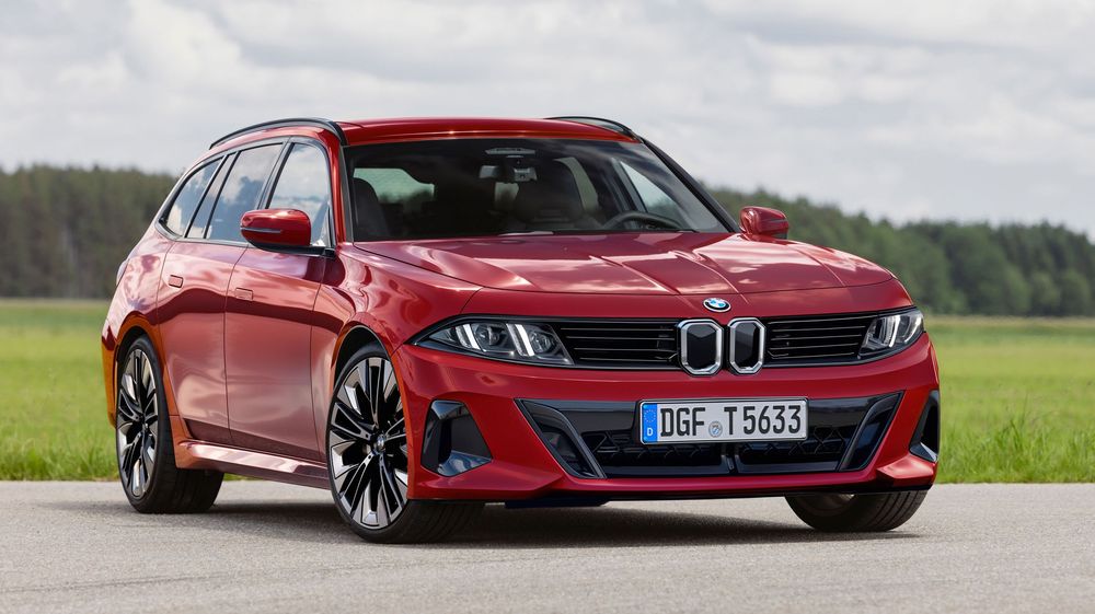 Red BMW 3 Series Touring wagon sits in a green field under cloudy skies showing its sporty front-end design and profile.