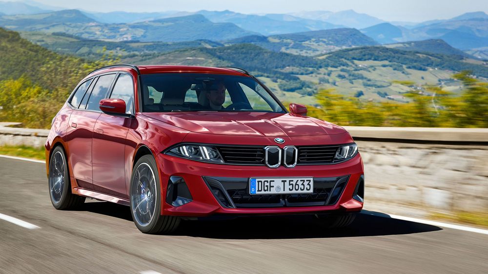 Red BMW 3-series station wagon drives on a winding mountain road against a scenic mountain landscape backdrop.