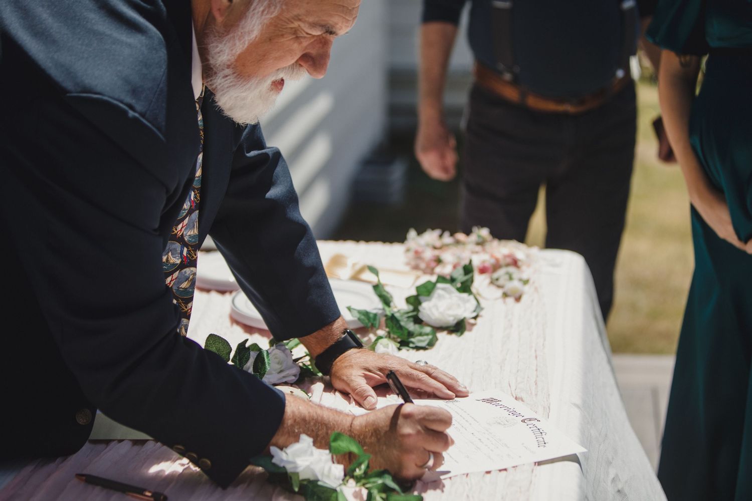 Someone signs a document at a table decorated with delicate white flowers at what appears to be a wedding ceremony.