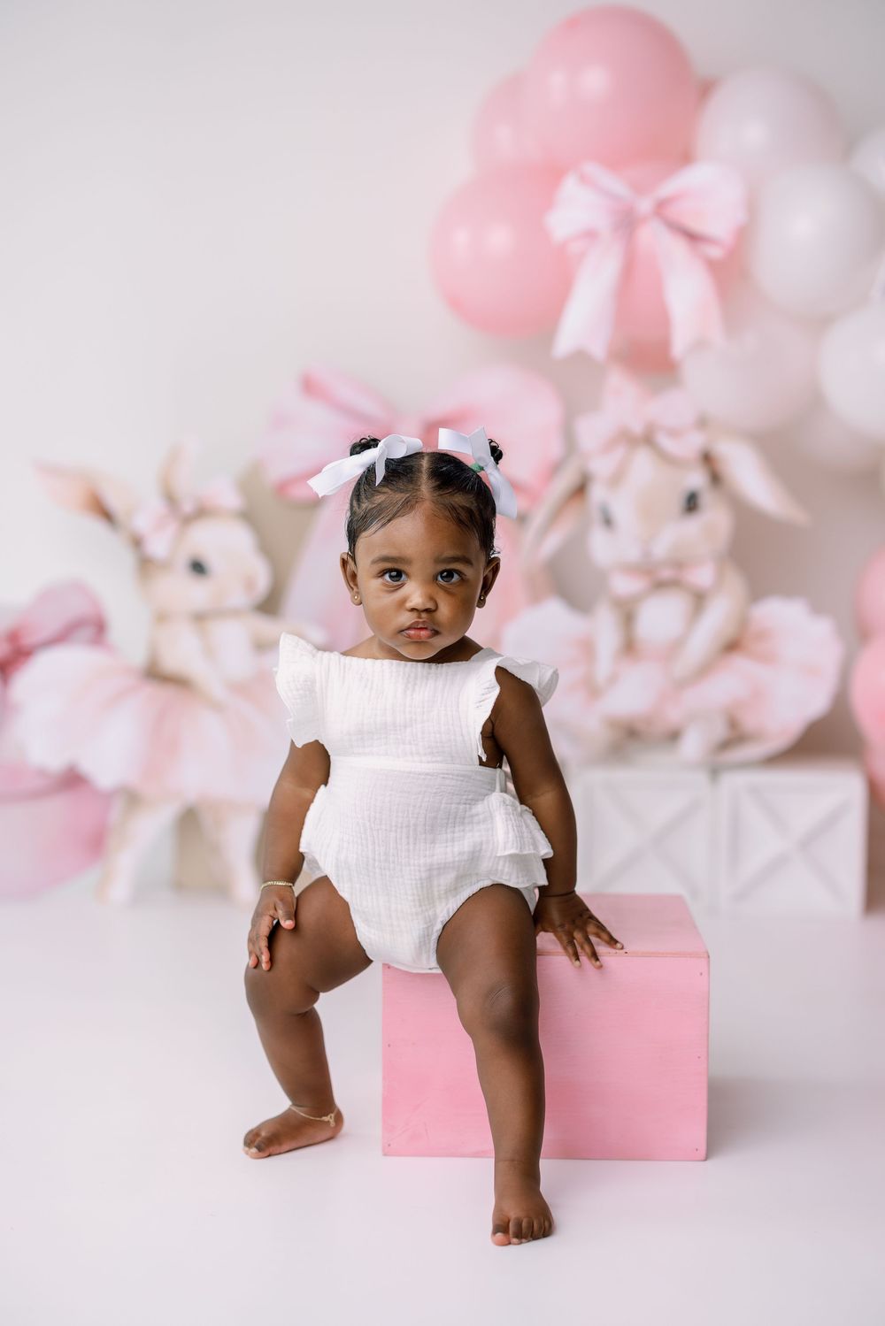 Sweet portrait setup with pink and white balloons, stuffed bunnies, and a pink box against a light background.