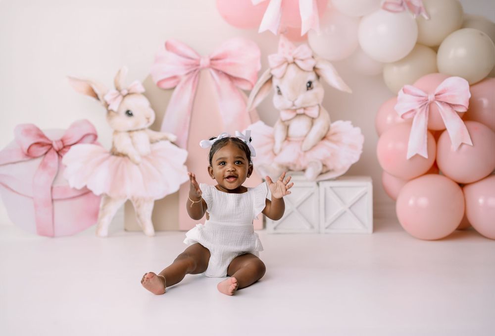 Pink and white baby photography backdrop with bunnies, bows, and balloons creating a sweet nursery scene.