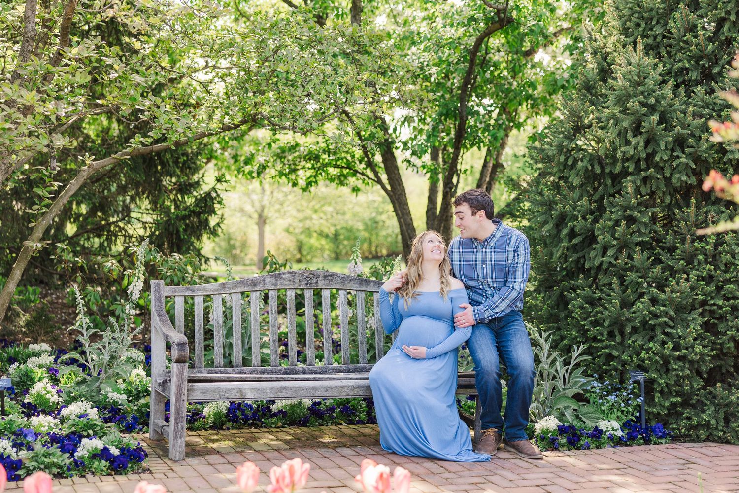 Two people sit together on a rustic wooden bench surrounded by lush garden greenery and purple flowers at Chicago Botanic Garden