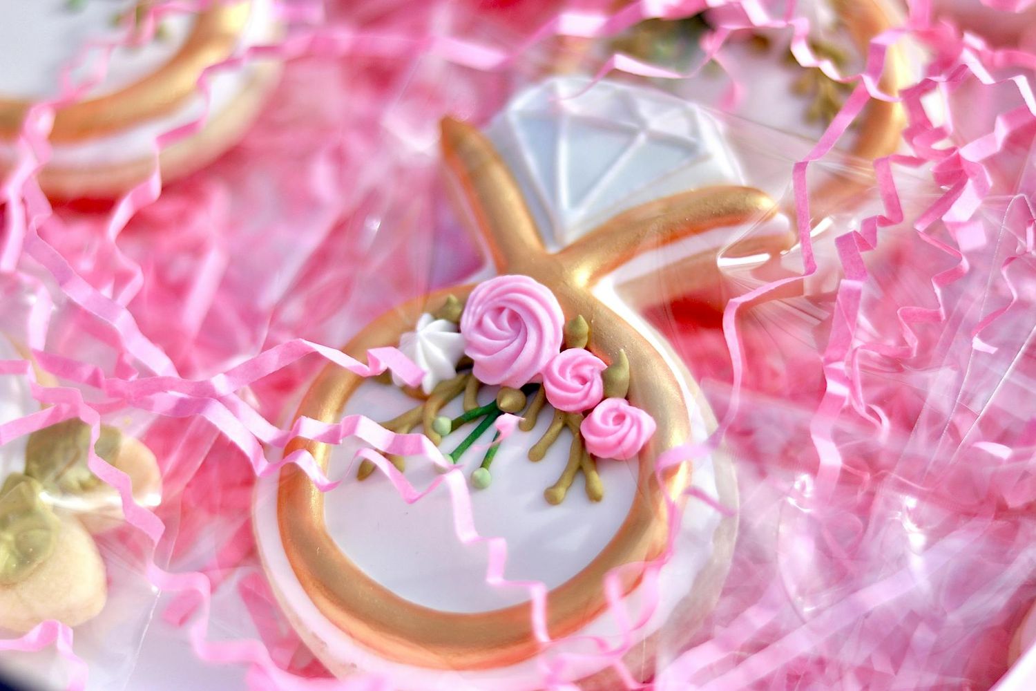 Delicate pink wedding ring cookies decorated with tiny floral icing details rest on a soft pink surface.