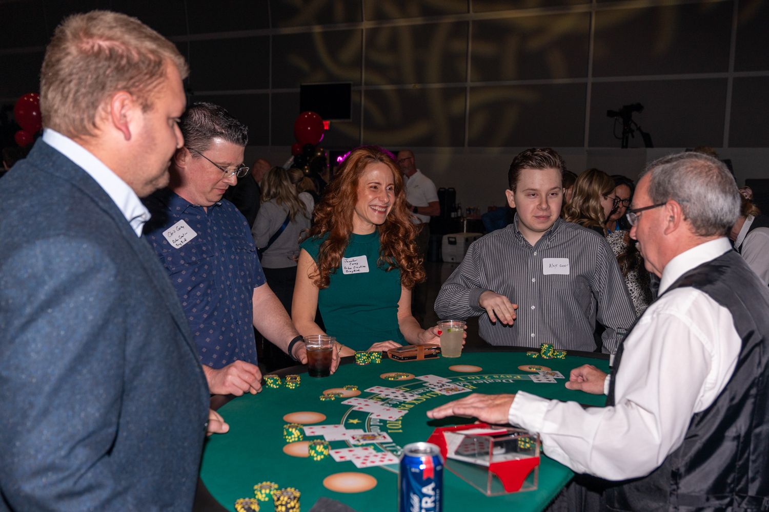 People gather around a green felt poker table with chips and cards during a casino night event.