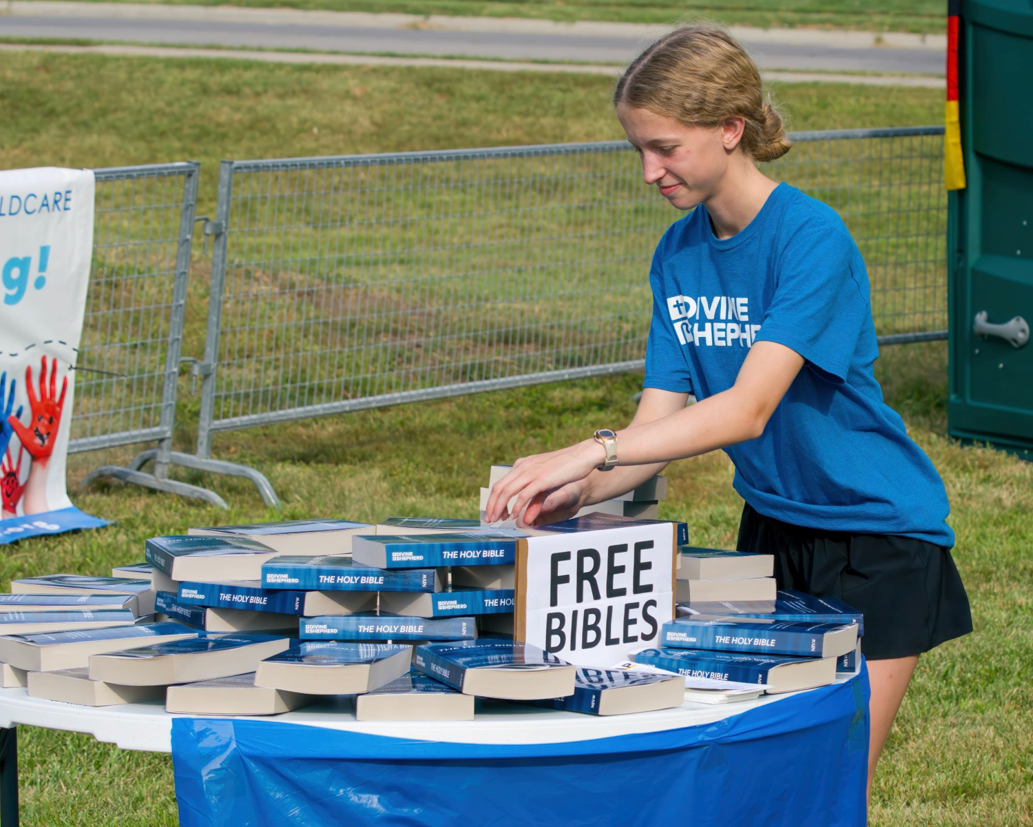 Volunteer at outdoor event staffing table offering free bibles at community gathering.