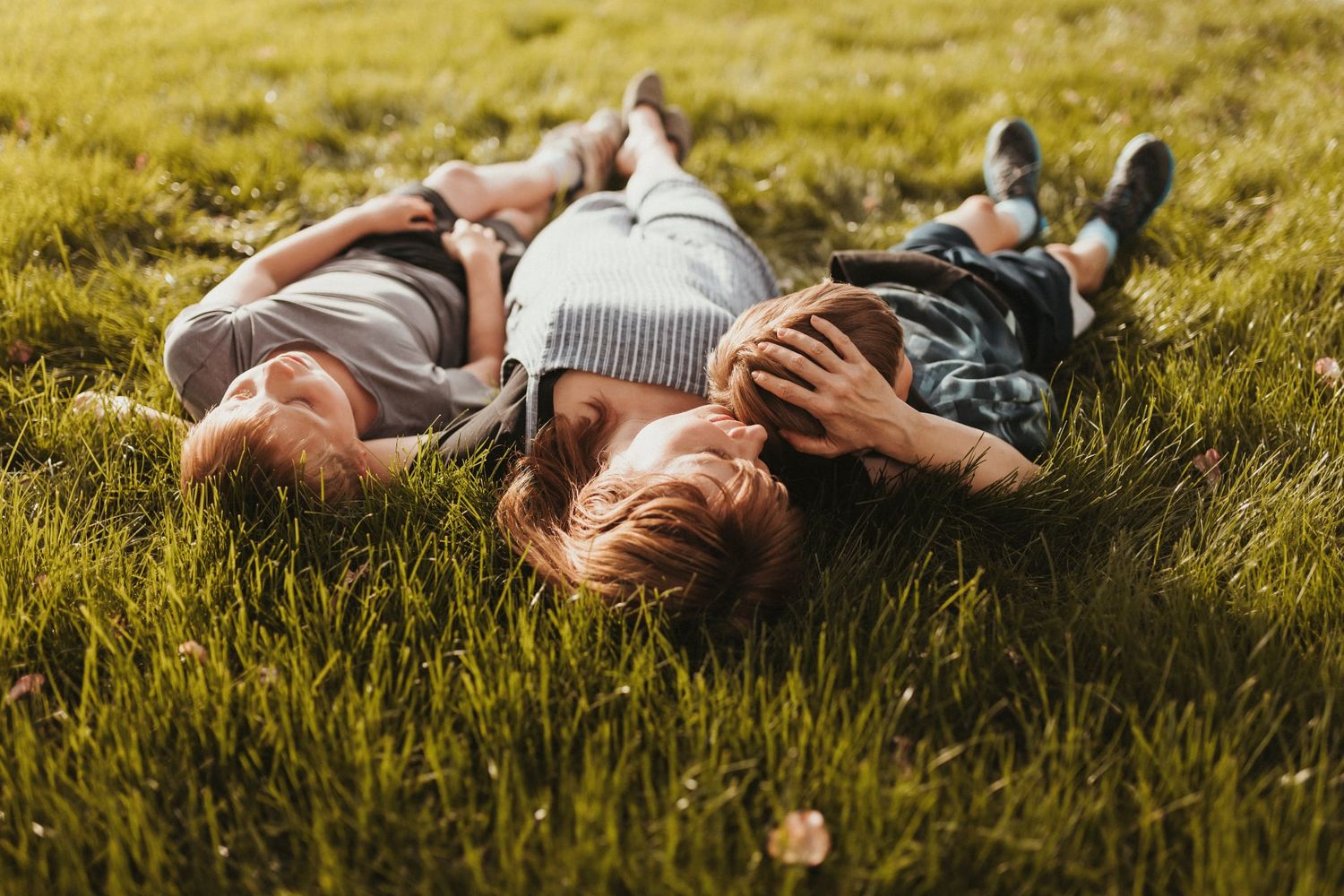 a mother lays on the grass with her two sons. They cuddle and look up at the sky. Family photos at home. Surrey. Elizabeth Lang Photography.