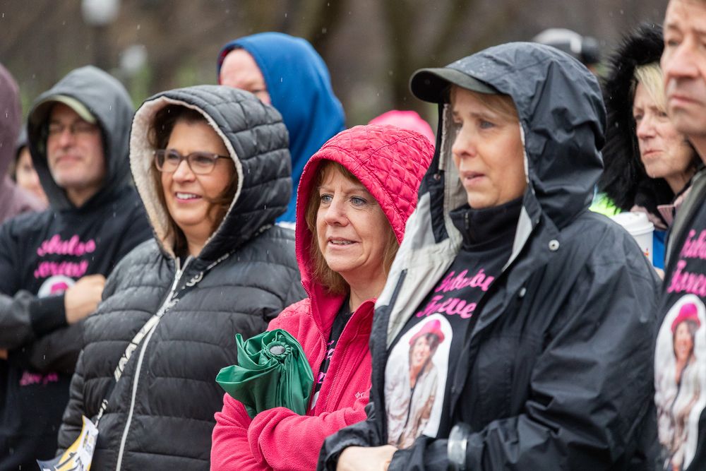 People wearing rain gear and warm winter clothing stand bundled up together in cold wet weather conditions.