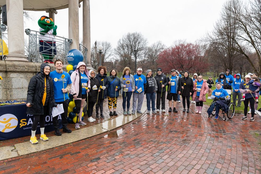 Crowd of marathon participants lined up at starting point under stone gazebo on rainy brick pathway.