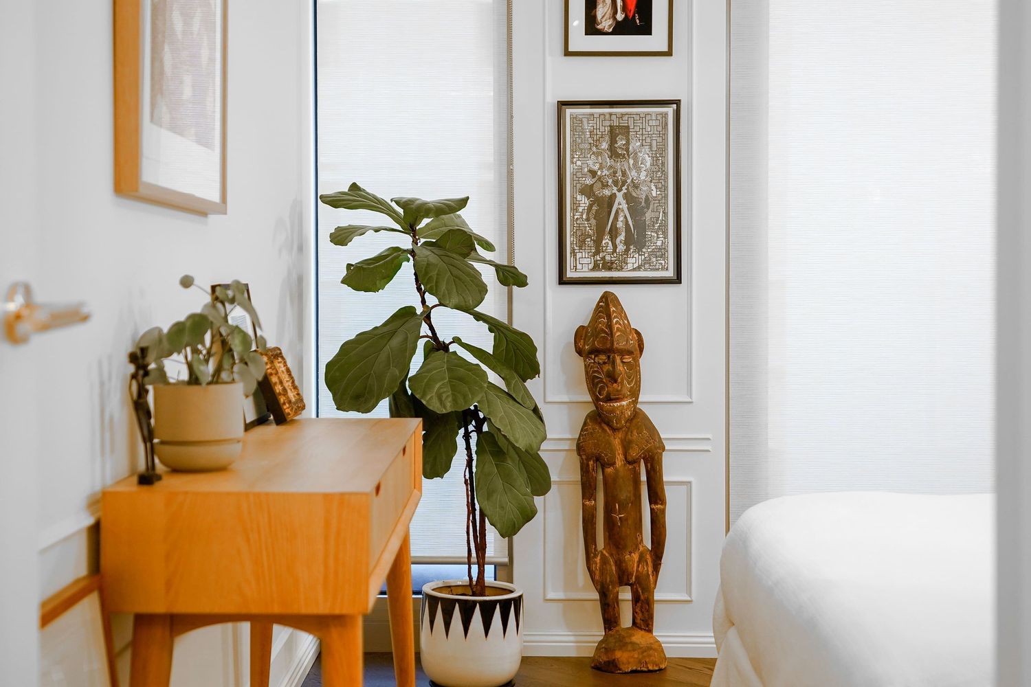 Mid-century modern furniture with a potted fiddle leaf fig plant and wooden tribal statue in a bright white room.