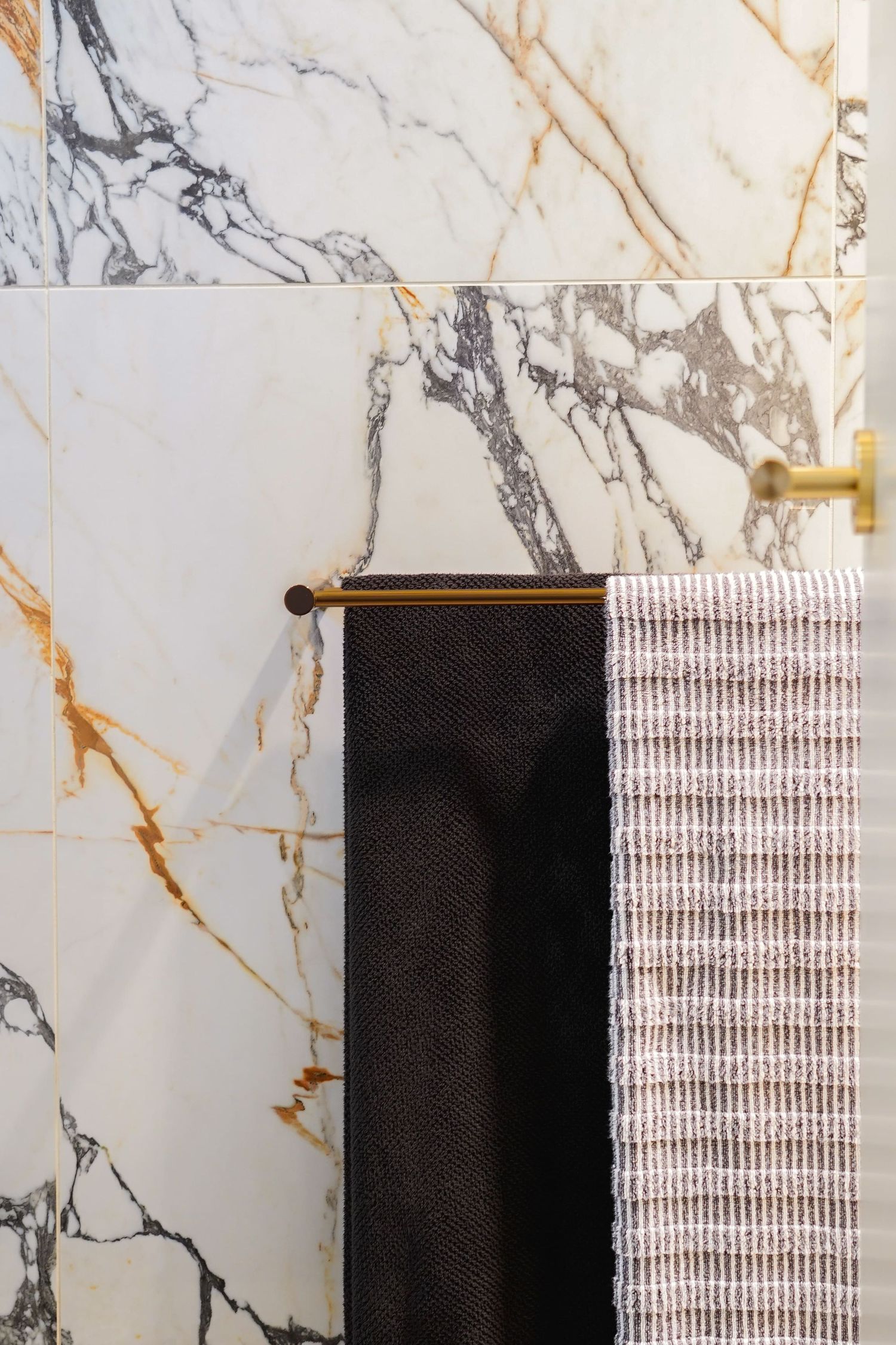 Close-up of black and white hand towels hanging on a gold bar against luxurious white marble wall with gold veining.