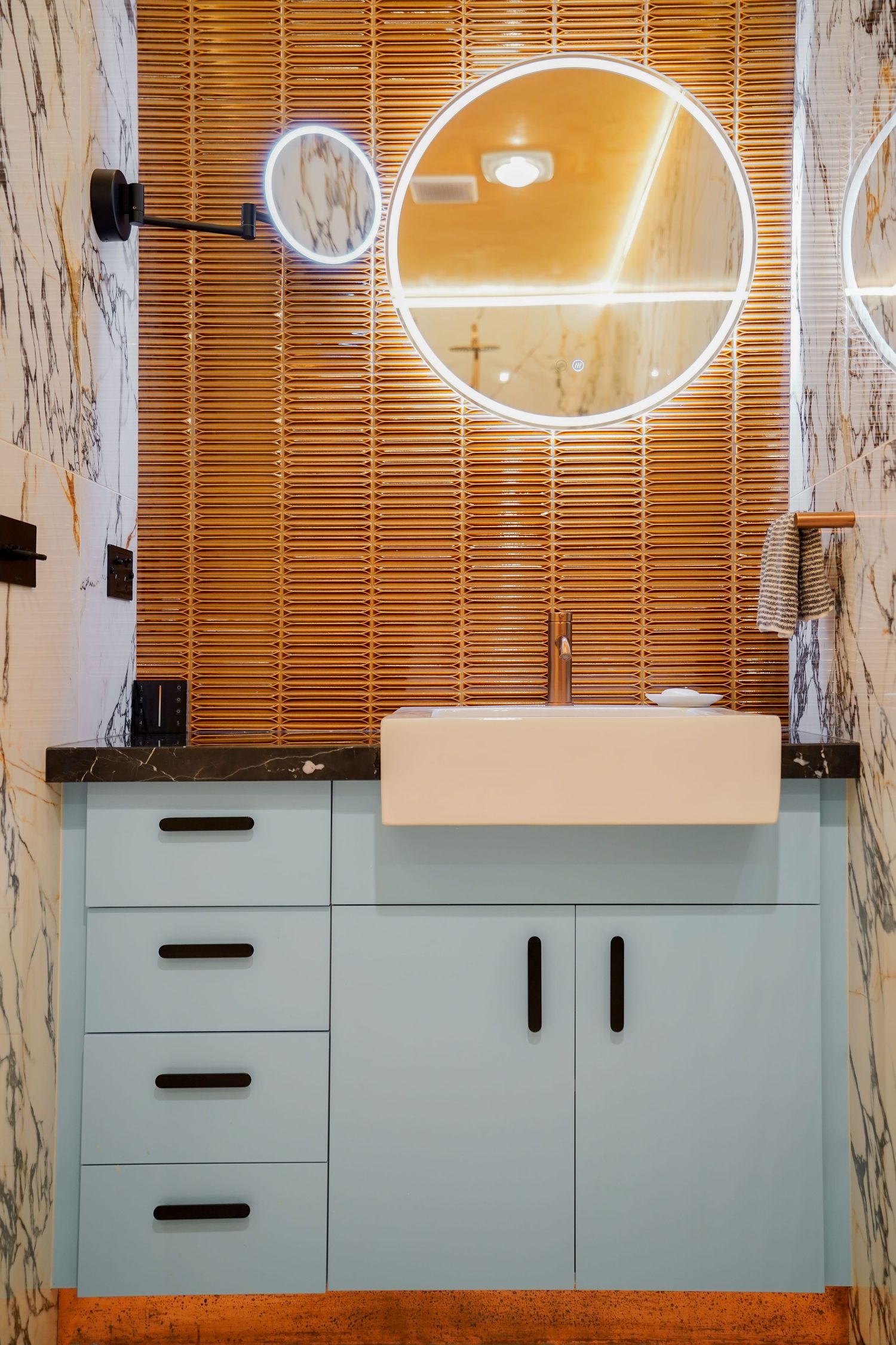 Modern bathroom vanity with light gray cabinets, vessel sink, and illuminated circular mirror against bamboo blinds.